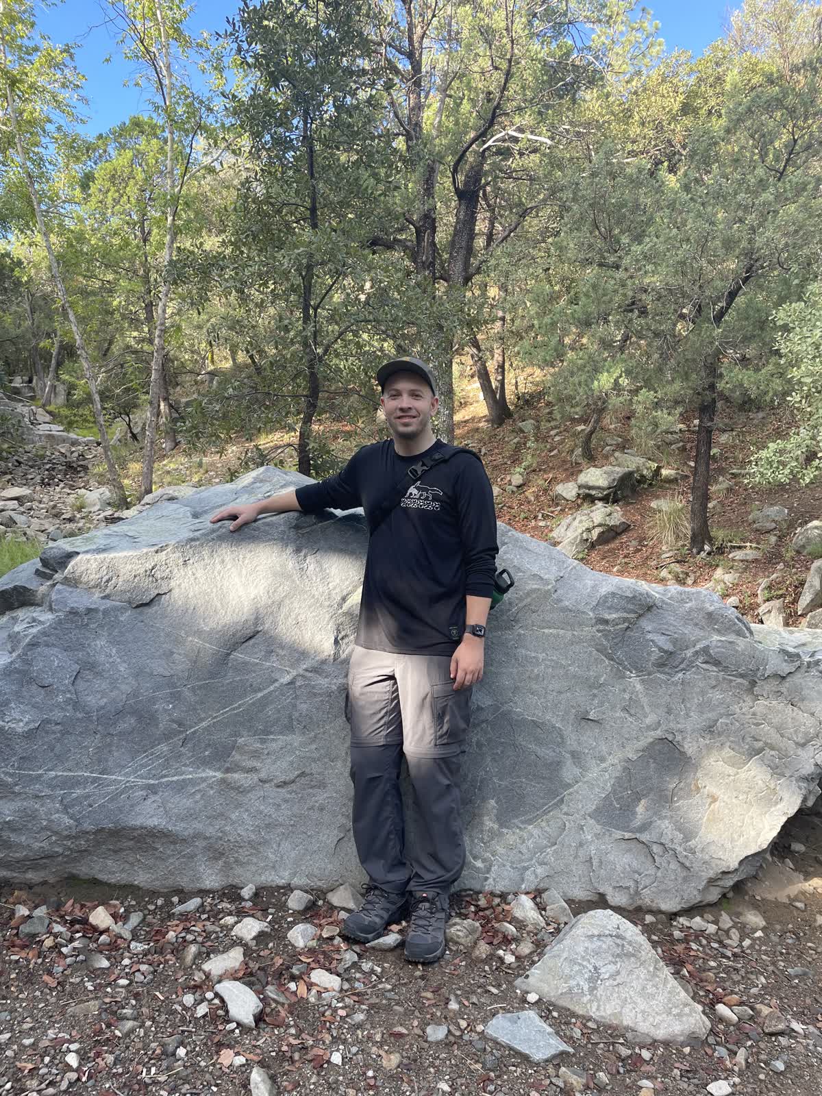 Ben standing beside a boulder on a wooded hike